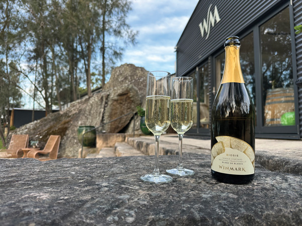 Bottle of Biosis Blanc de Blancs and two sparkling wine glasses outside Winmark Cellar Door
